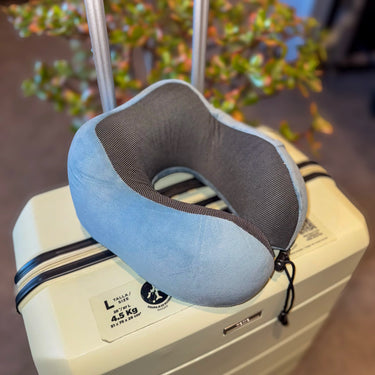 Coussin de voyage à mémoire de forme bleu posé sur une valise, idéal pour un confort optimal en déplacement. Accessoire ergonomique et pratique pour les voyageurs.